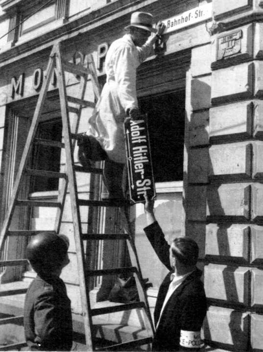 Arbeiter entfernen die Beschilderung an der ehemaligen Adolf-Hitler-Straße (heute Steinbrückstraße) in Trier, 12. Mai 1945. Foto: US Army - Public Domain