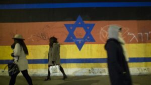 Menschen vor einem Wandgemälde, das eine Kombination aus der israelischen und der deutschen Flagge an der Berliner Mauer zeigt. 13. März 2016. Foto: Noam Revkin Fenton/FLASH90